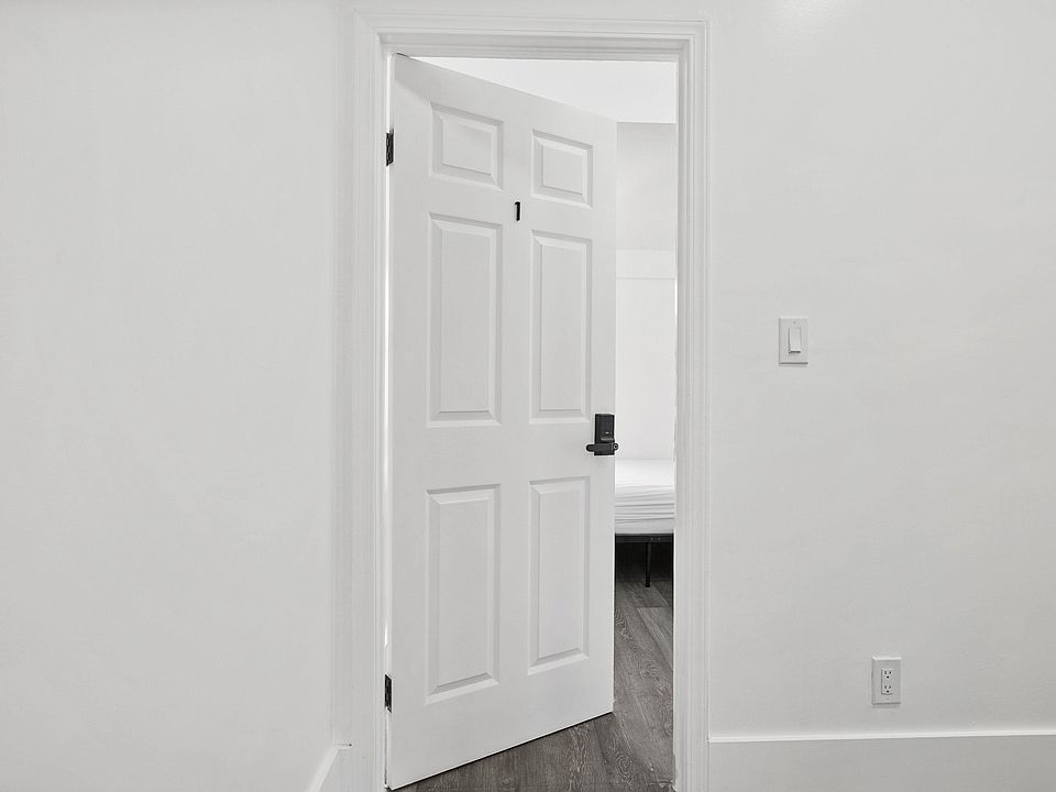 Entry hallway with fresh white walls, paneled door, and durable wood-look flooring leading into the bedroom.