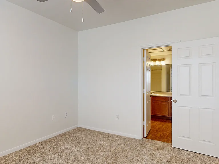 Spacious apartment bedroom with attached bathroom and plush carpet flooring.