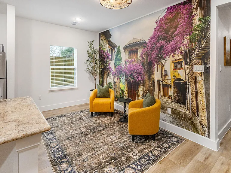 Chic seating nook off the kitchen with two accent chairs, statement mural, and a window with blinds for natural light.
