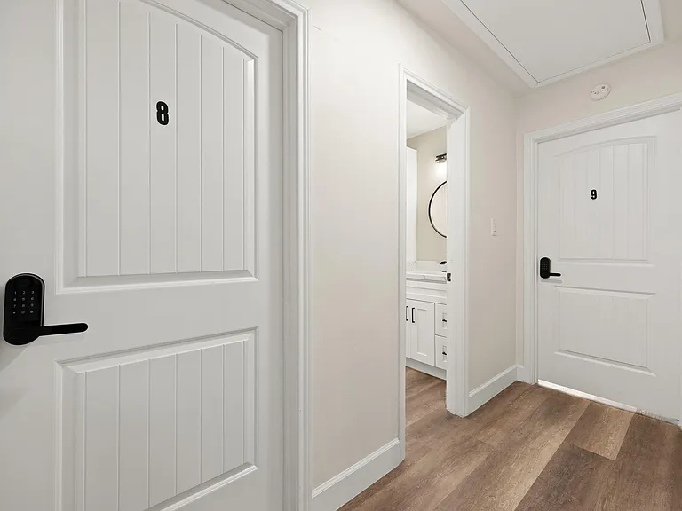 Clean interior hallway with wood-style flooring, recessed access panel, and nearby bathroom vanity for added convenience.