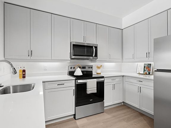 Renovated Package II kitchen with stainless steel appliances, grey cabinetry, white quartz countertops, and hard surface flooring
