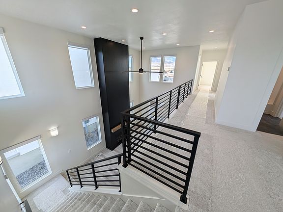 Modern upstairs hallway with white walls and carpet, black metal railings, large vertical windows, a