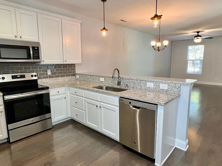 Spacious kitchen with modern white cabinets, granite counter tops, tile backsplash, stainless steel fridge, sink, oven/range, and microwave.