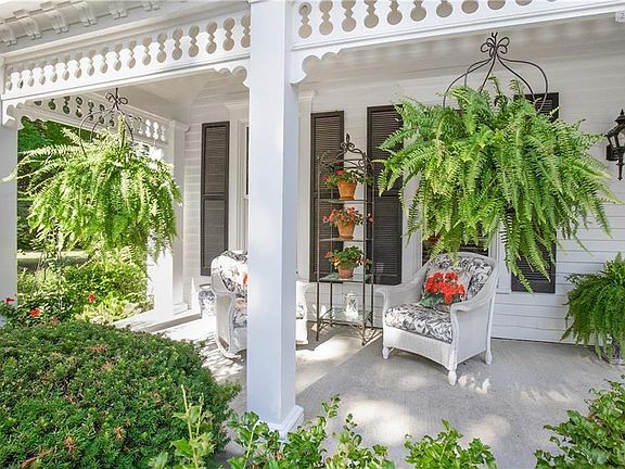 The covered front porch has views of the grounds and trees and manicured landscape