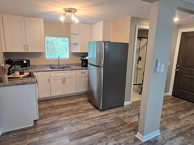 Efficient kitchen with ample white cabinetry, laminate counters, windowed sink, and full-size refrigerator for everyday use.