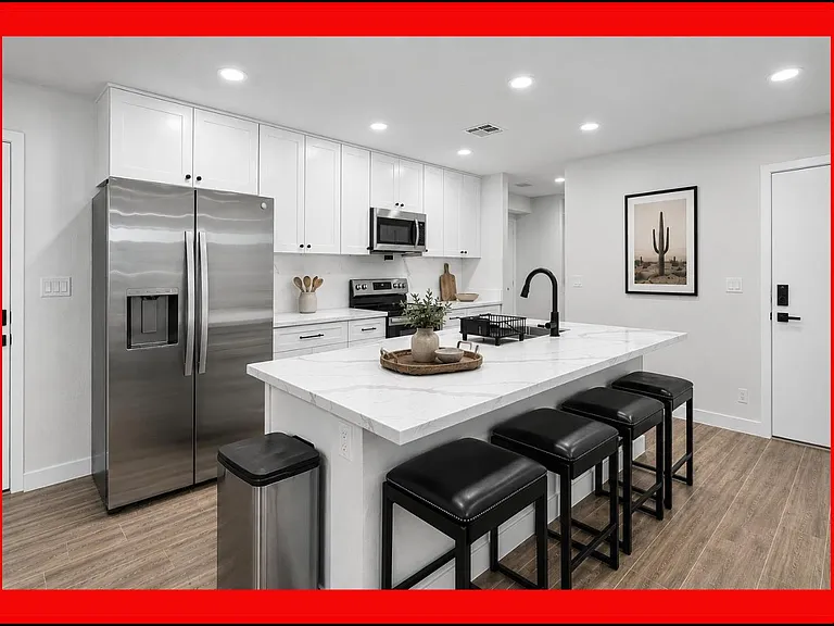 Spacious kitchen with a large quartz island, bar seating, and stainless-steel appliances plus ample white cabinetry.