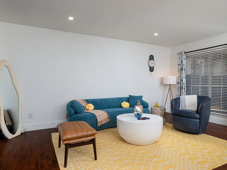 Relax in a bright and stylish living room featuring cozy blue seating, warm accents, and a modern round coffee table. Perfect for lounging, reading, or gathering with friends.
