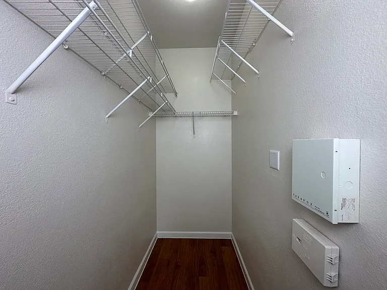 Spacious walk-in closet with wire shelving and sleek wood-style floors for organized storage solutions. Spacious walk-in closet with wire shelving and sleek wood-style floors for organized storage solutions.