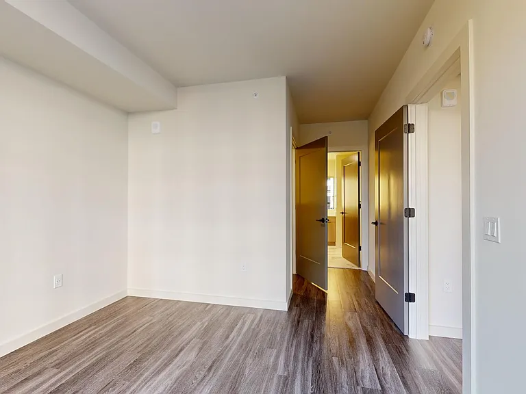 Spacious apartment bedroom with large closet, attached bathroom, and wood-style flooring.