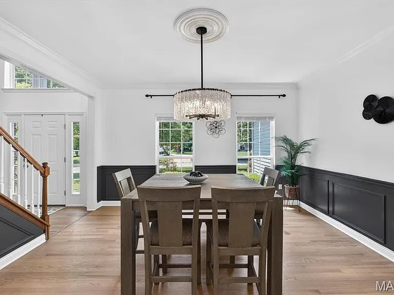 Spacious dining area featuring wood-finish flooring, wainscoting, and a decorative chandelier
