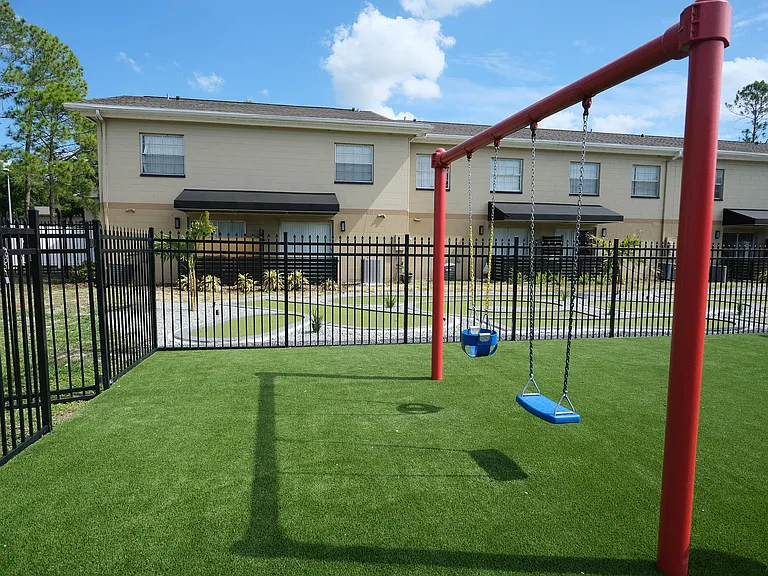 Charming community playground with vibrant red swings set against a backdrop of well-maintained townhouses, ideal for family-friendly living.