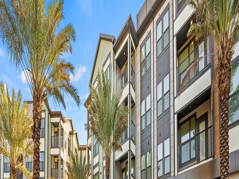 Luxurious apartment complex with sleek modern design featuring a sparkling outdoor pool surrounded by palm trees and comfortable lounge chairs.