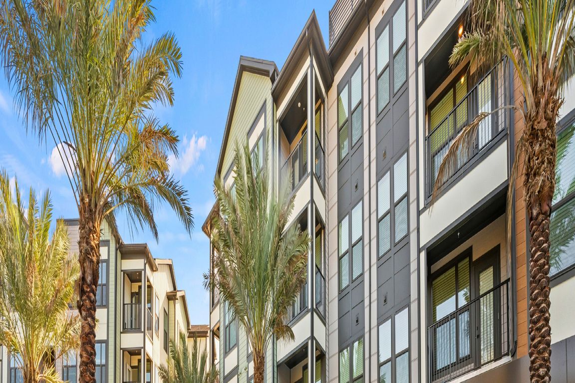 Luxurious apartment complex with sleek modern design featuring a sparkling outdoor pool surrounded by palm trees and comfortable lounge chairs.