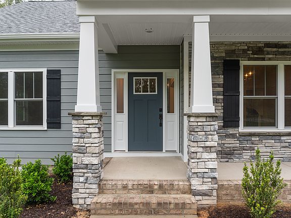 Front porch of a house with stone columns, a blue front door with sidelights, and gray siding. The p