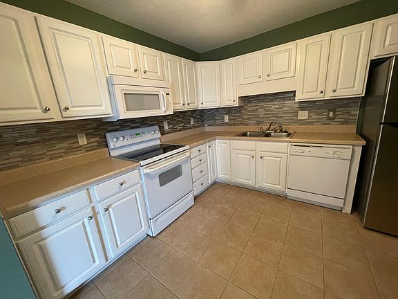 Kitchen with smooth surface cooktop/oven, microwave, dishwasher and stainless steel refrigerator. Glass tile backsplash.