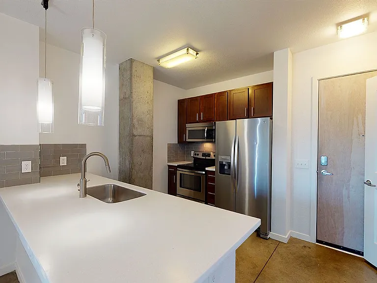Apartment kitchen with stainless steel appliances, quartz countertops and polished concrete flooring.