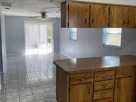 View of kitchen cabinets looking into living room area highlighting dual ceiling fans, side windows and sliding glass doors to patio