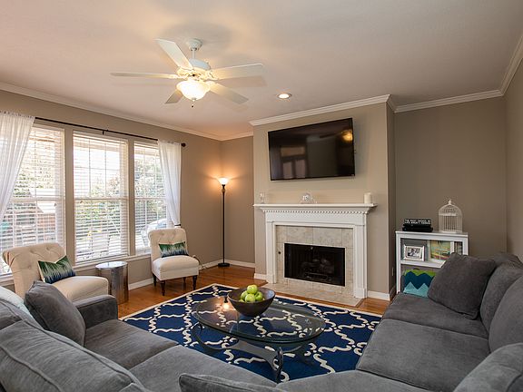 Open family room with hardwoods, crown moulding, ceiling fan and gas fireplace with decorative mantle. 