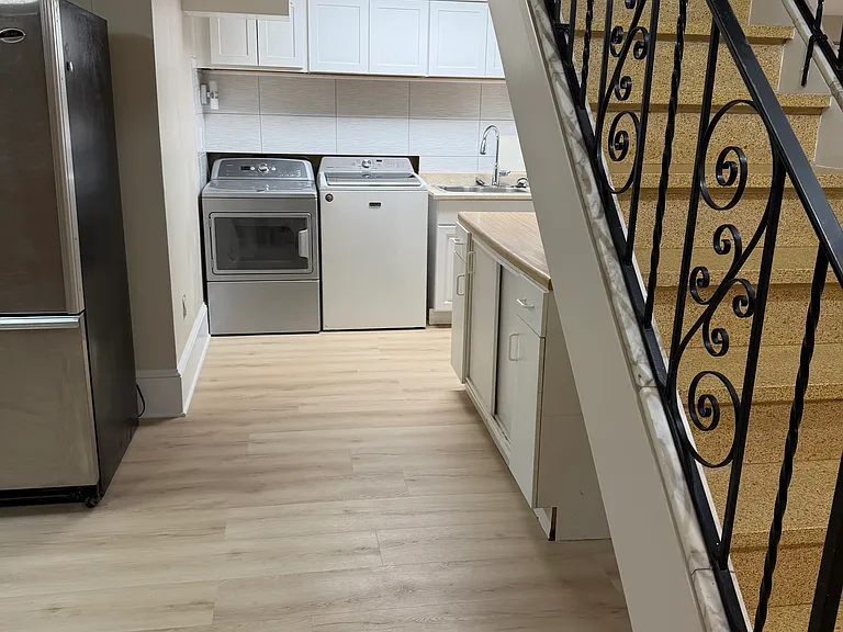 Lower-level laundry room with full size washer and dryer, new wall cabinetry, sink base, and plumbing. Food prep cabinetry/laundry folding area shown on the side of the photo under the staircase. 2nd refrigerator on left in table area.