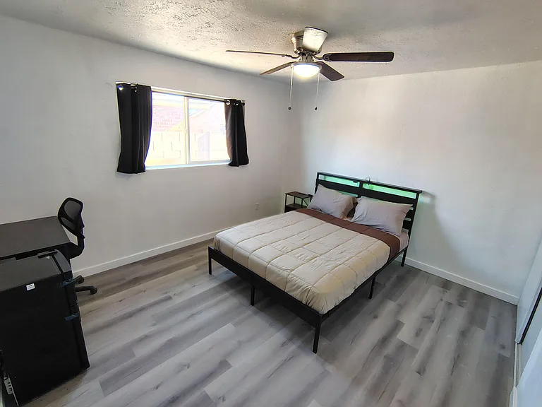 Furnished bedroom with a ceiling fan, window with curtains, and space for a desk or seating area.
