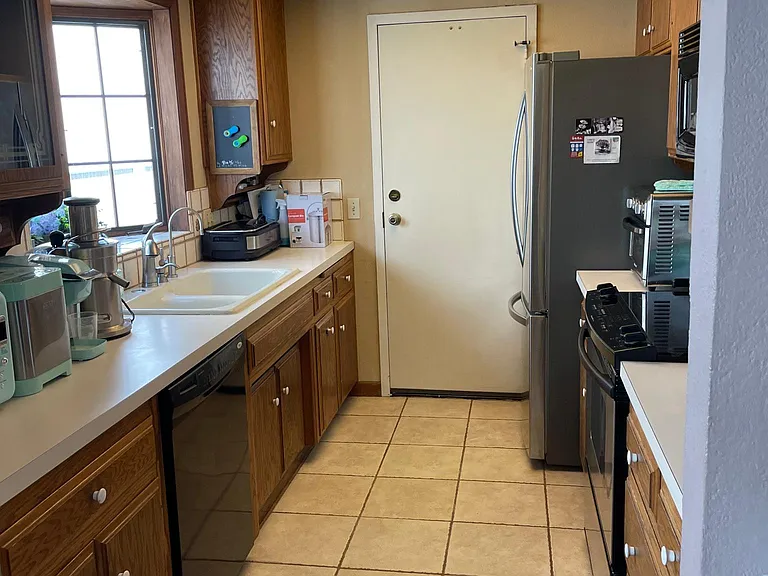 Galley kitchen with appliances. Electric stove, microwave, stainless refrigerator.
Kitchen countertops will be replaced by Silestone (engineered quartz) before occupancy.