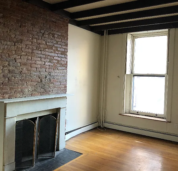 Light-filled living room with historic brick accent wall and fireplace. Facing Walnut St.
