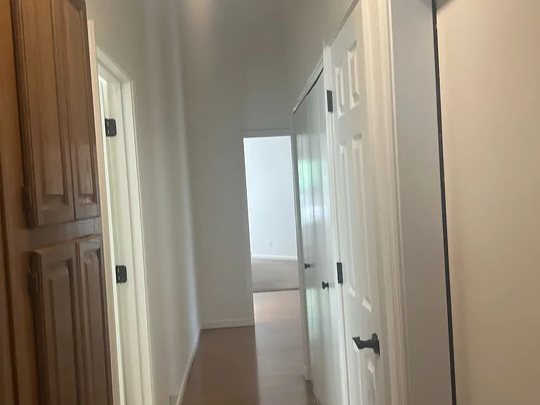 Hallway leading from the second bedroom towards the primary bedroom. On the left is the linen closet and bathroom. On the right is the garage door, coat closet, and laundry room.