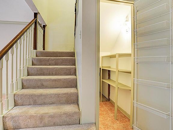 Large pantry with plenty of storage space next to stairs leading upstairs to bedrooms.
