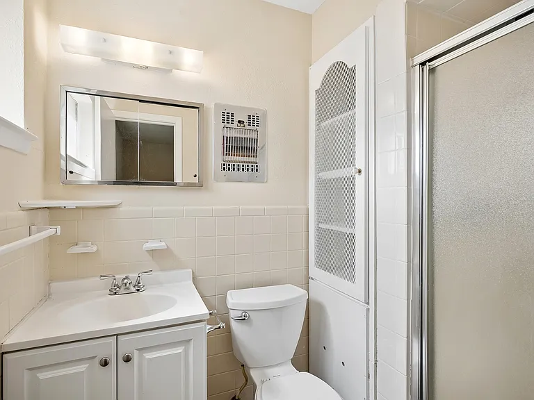 This is the ensuite (private) primary bath with a shower, linen cabinet with vintate doors and vanity with storage space below.
