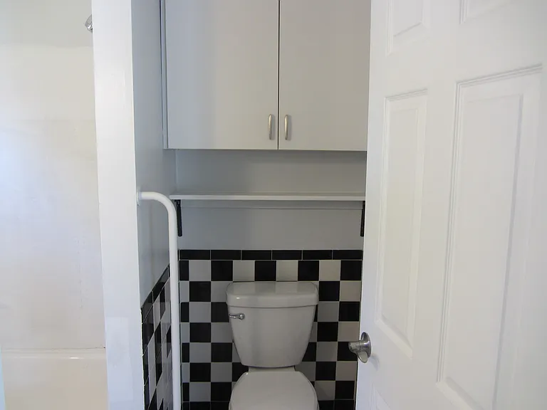 Bathroom with storage cabinet and shelf above toilet.
