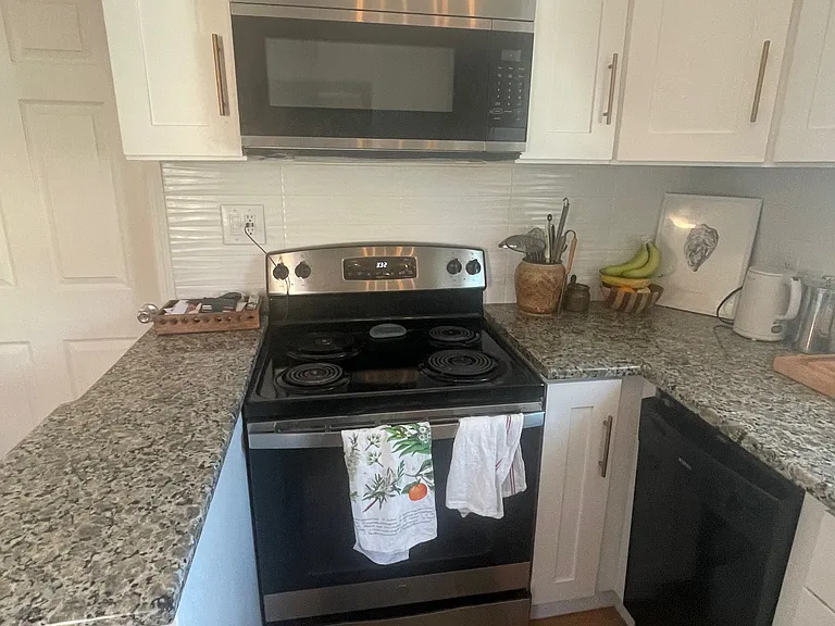 Kitchen has electric stove with built-in microwave, and dishwasher. Granite countertops with white shaker cabinets.