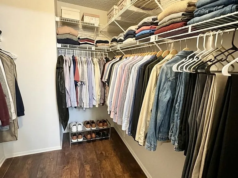 Walk-in closet with wraparound wire shelving, double hanging rods, and open floor space for shoes and storage bins.