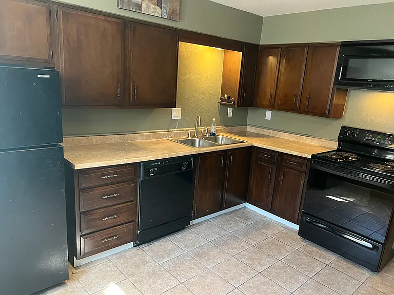 Kitchen dark cabinets, double sink, dishwasher, self-clean oven, microwave, dishwasher, and refrigerator.