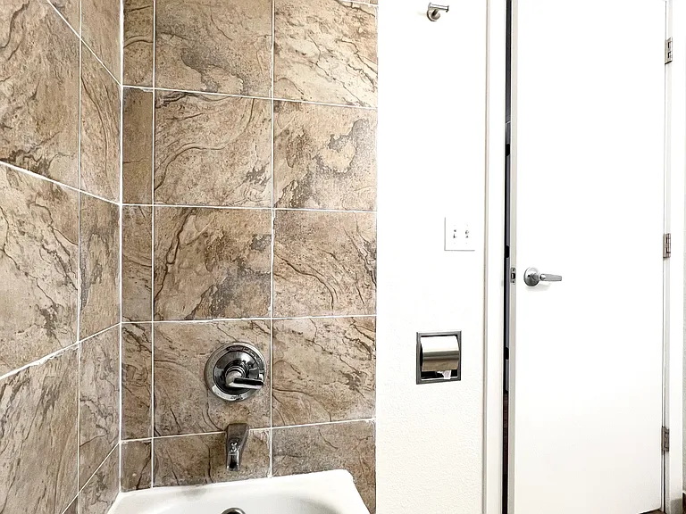 Bathroom shower/tub with rain shower and built in fixtures for toilet paper, towel hangers, storage.