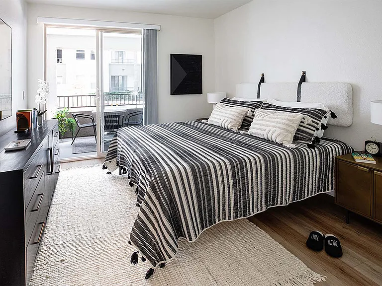 Spacious apartment bedroom with wood-style flooring and balcony access.