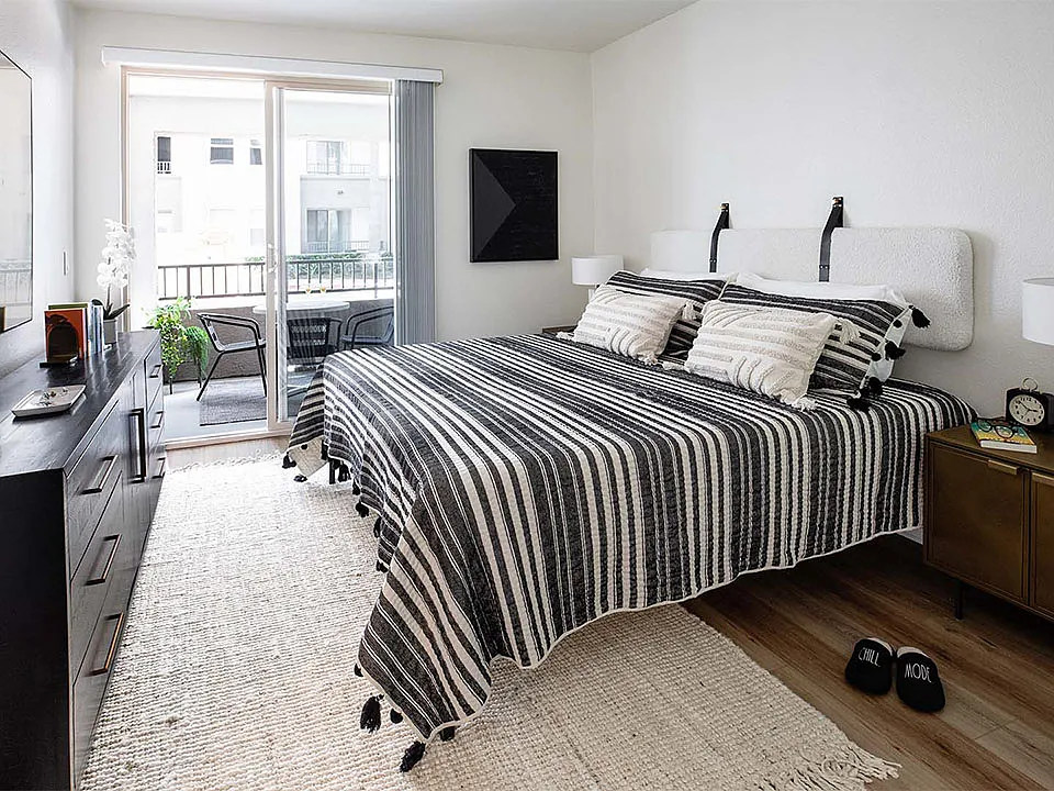 Spacious apartment bedroom with wood-style flooring and balcony access.