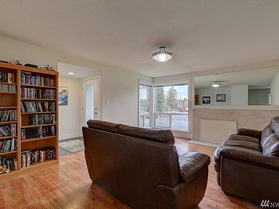 Large living room with beautiful wood floors, a large mirror and tile fireplace adjacent to the wrap around corner windows.