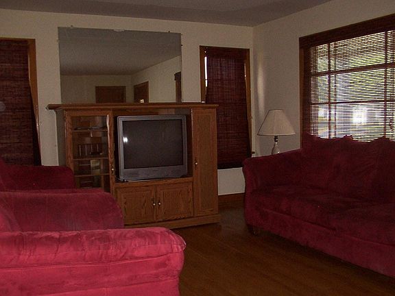Living room with microfiber suede furniture, hardwood floors, Roman blinds, entertainment center with TV, desk.