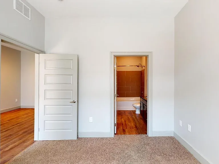 Spacious apartment bedroom with attached bathroom and plush carpet flooring.
