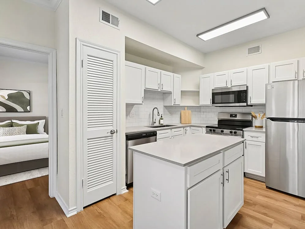 Renovated Package I kitchen with stainless steel appliances, white cabinetry, white tile backsplash, grey quartz countertops, and hard surface flooring - eaves North Dallas