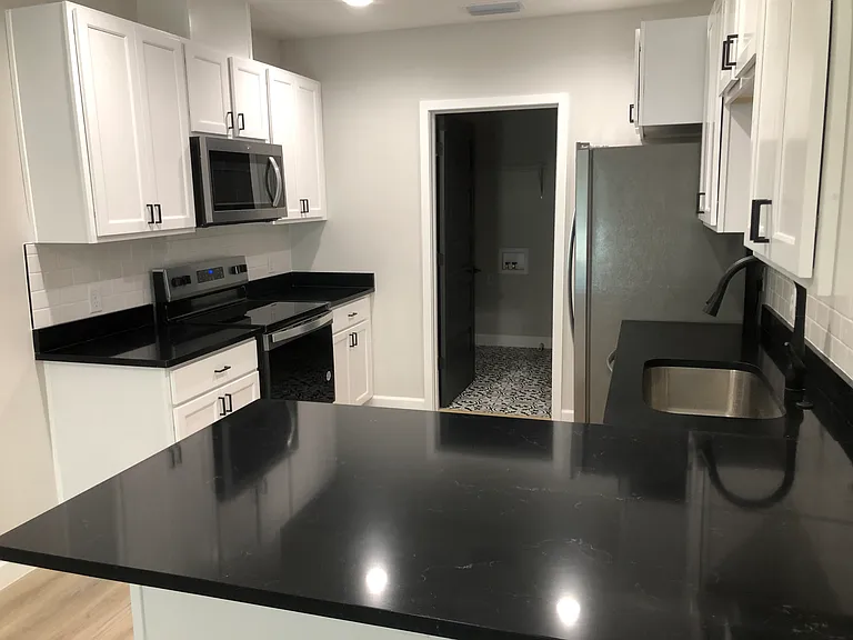 Kitchen with stainless steel appliances and black quartz. White subway backsplash, and sink deposal