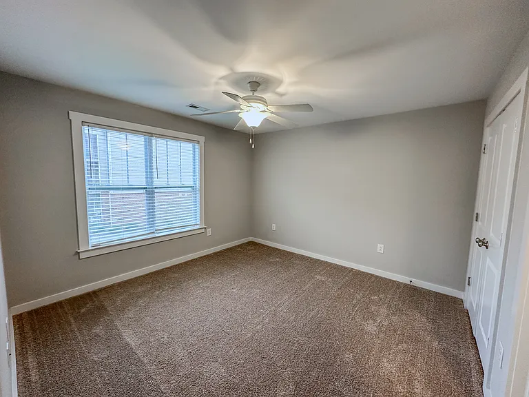 The bedroom features a large window, ceiling fan, large double door closet, and a door to the bathroom.