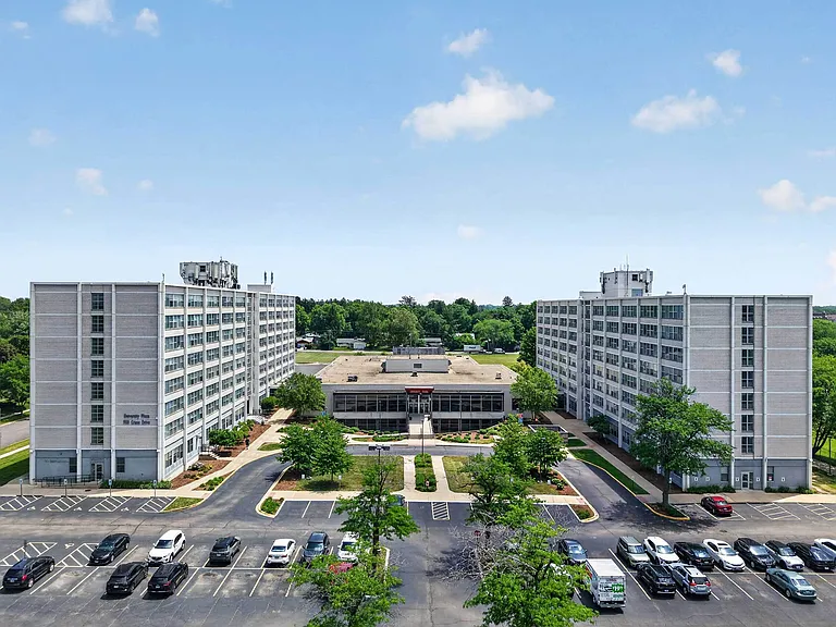 Impressive aerial view of modern apartment complex with twin high-rise buildings and lush greenery, ample parking space, and inviting pathways.