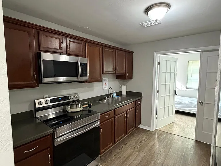 Efficient galley kitchen with ample cabinet storage, solid-surface counters, and stainless microwave over an electric range.