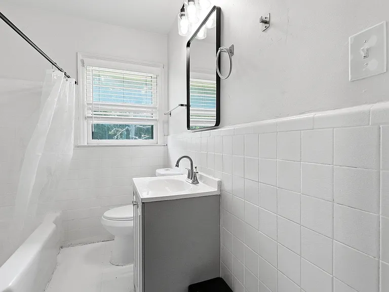 Clean full bathroom with tub/shower combo, tile surround, vanity sink, and a window with blinds for natural light.