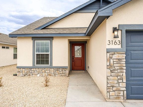 Single-story house with beige siding, stone accents, a red front door, and a two-car garage. The dri