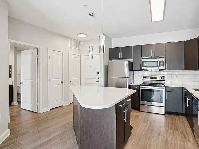 Experience contemporary living in this stylish kitchen featuring an island, quartz countertops, and stainless steel appliances at Addison Keller Springs in Addison, TX.