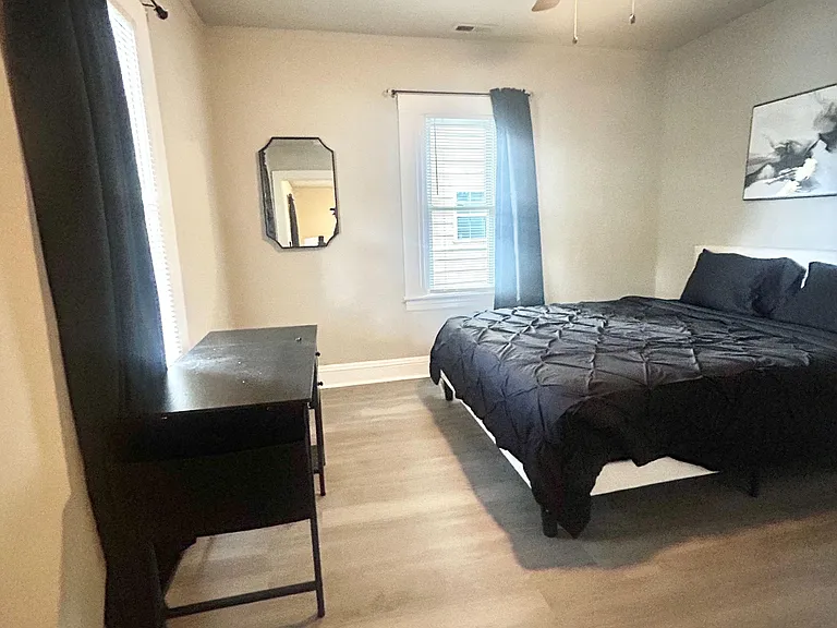 Spacious bedroom with a ceiling fan, two windows with blinds, and room for a bed plus a dresser or desk setup.