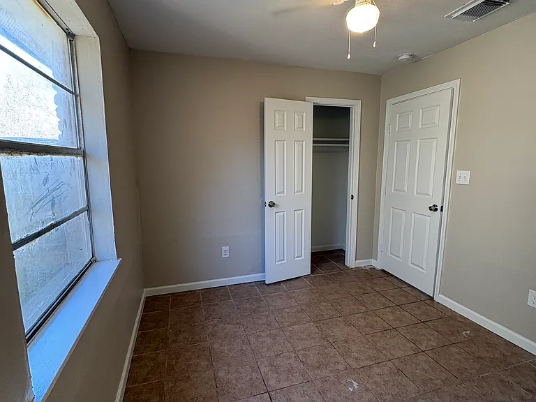 First bedroom with a closet and ceiling fan. Large window for natural light leading to the back yard.