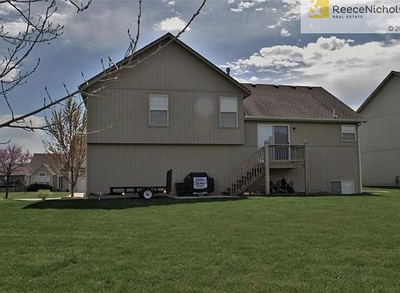 Back of home with patio and flat yard and tree.